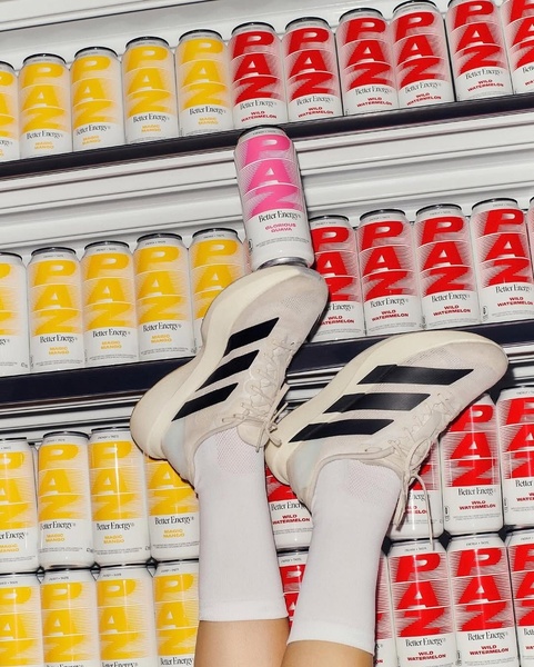 A high-contrast, vertical-format ad creative featuring a single energy drink can balanced on a shoe, surrounded by a symmetrical shelf of product inventory.